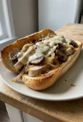 A close-up of a chicken cheesesteak sandwich filled with meat, peppers, and cheese.