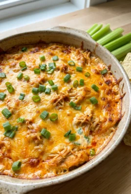 A close-up of a scoop of baked chicken wing dip on a tortilla chip.