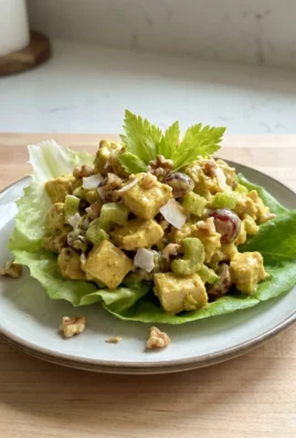 A close-up of a spoon scooping curry chicken salad from a large glass bowl.