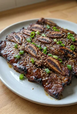 A close-up of grilled Korean short ribs with visible bone sections on a white plate.