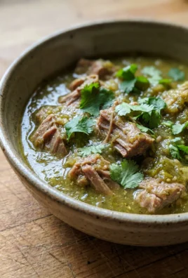 A close-up of a spoonful of pork chili verde showing tender meat and green sauce.