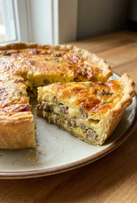 A slice of sausage quiche on a white plate next to a fork.