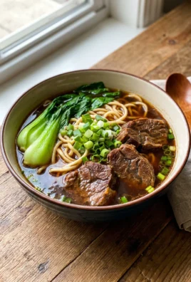 A close-up of a steaming bowl of beef noodle soup showing noodles and beef.